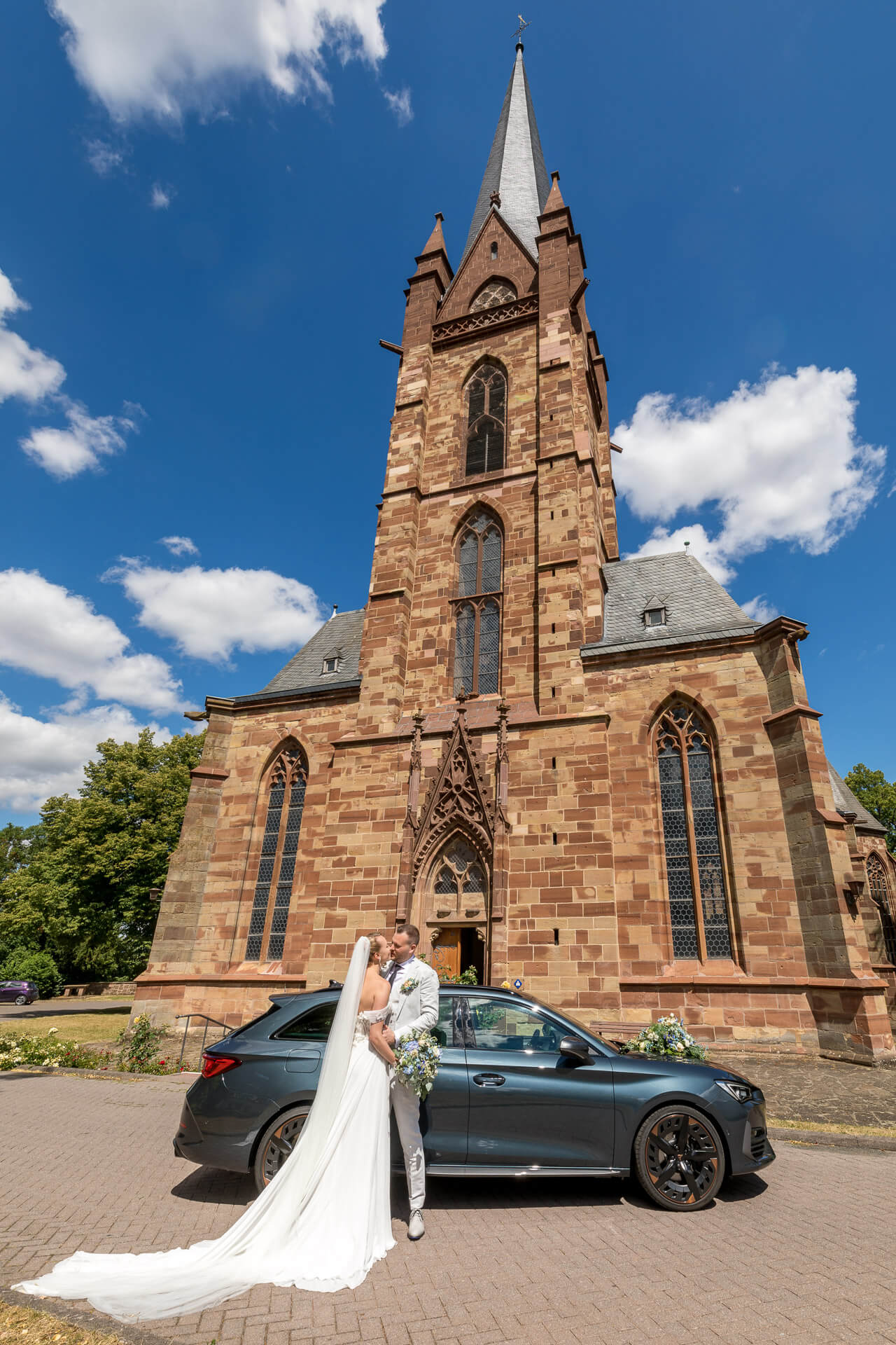 Kussfoto vom Brautpaar vor der Kirche mit dem Auto