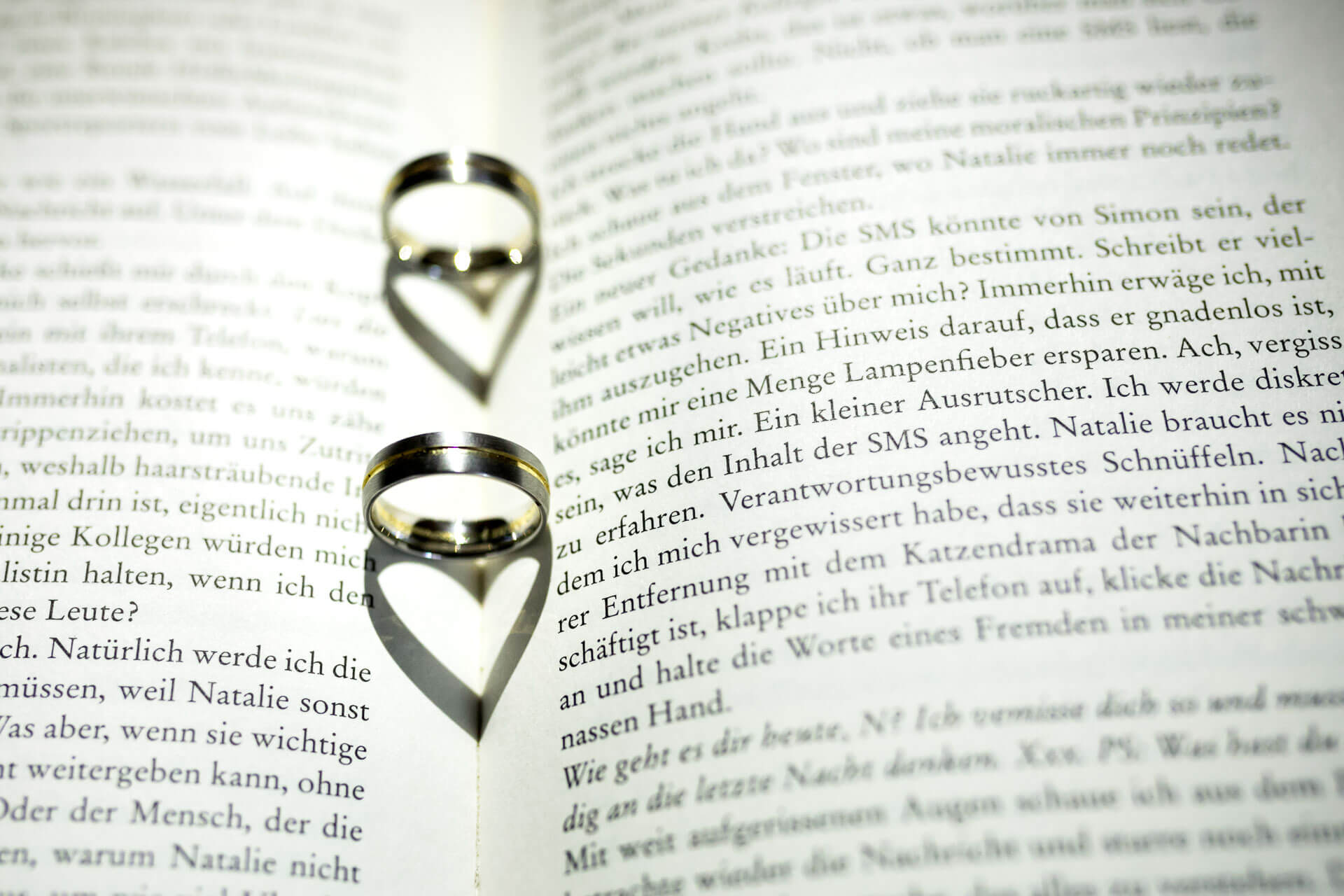 Ringe liegen auf einen Buch und der Schatten zeigt zwei Herzen.