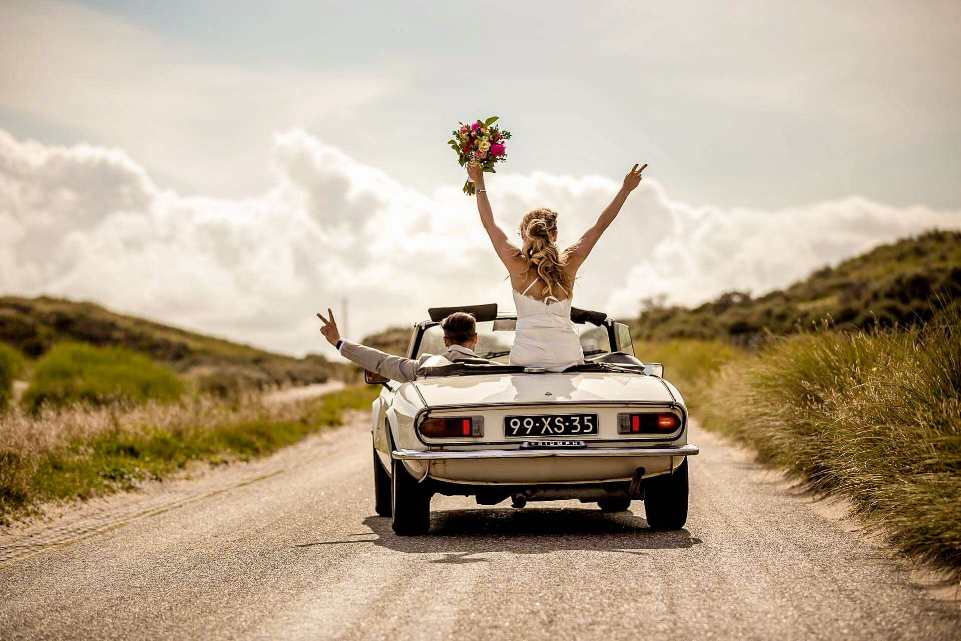 Braut im Cabrio Braut steht jubelnd mit dem Brautstrauß in einem Oldtimer-Cabrio auf einer Landstraße
