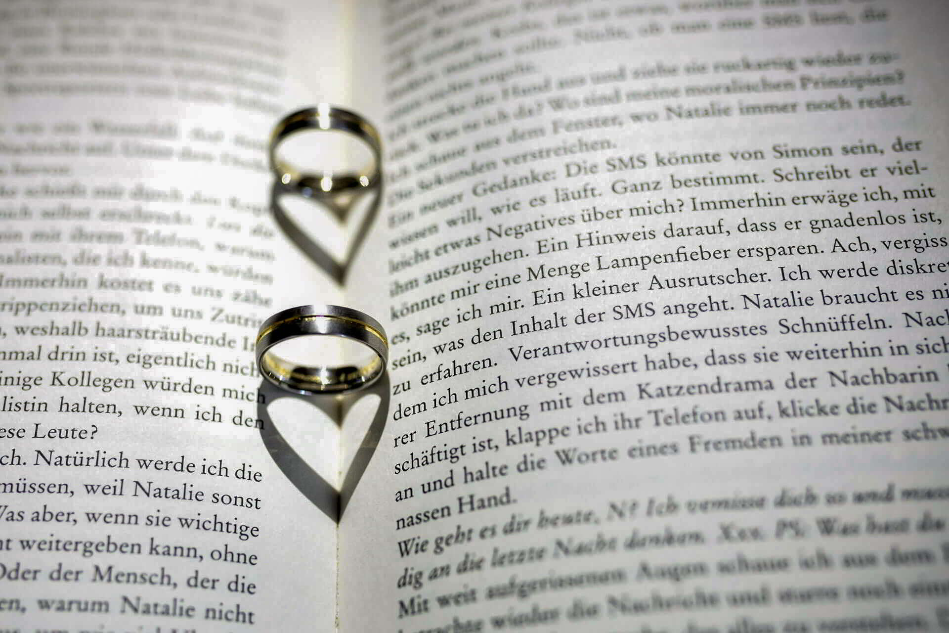 Eheringe im Buch Eheringe auf einem aufgeschlagenen Buch, deren Schatten ein Herz bildet